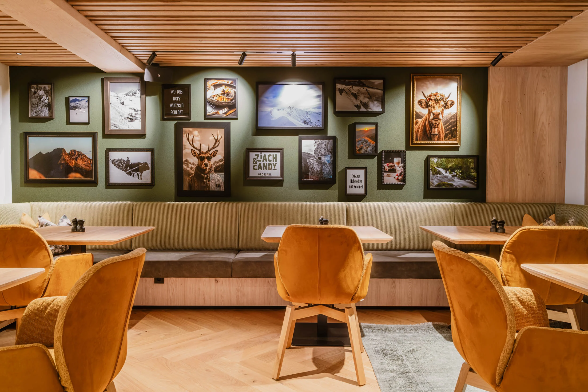 Polstersitzreihe des Restaurants. An der grünen Wand hängen viele Bilder mit Hirschen, Murmeltieren